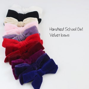 May include: A collection of hand-tied velvet bows in various colors, including white, black, beige, pink, purple, red, burgundy, and deep blue. The bows are arranged in a diagonal line, with the text "Handtied School Girl Velvet bows" visible.
