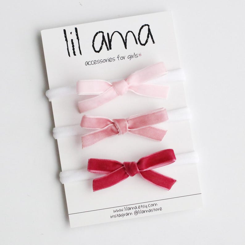May include: Three velvet hair bows in shades of pink and red, displayed on a white card with the text "lil ama accessories for girls".