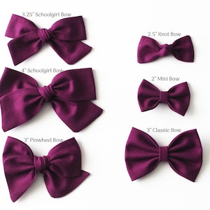 May include: A collection of six different-sized, deep purple fabric bows on a white background. The bows include a 3.25-inch Schoolgirl Bow, a 4-inch Schoolgirl Bow, a 3-inch Pinwheel Bow, a 2.5-inch Knot Bow, a 2-inch Mini Bow, and a 3-inch Classic Bow.