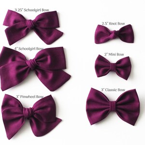 May include: Five different sizes of burgundy fabric hair bows. The bows are labeled with their size and type: 3.25" Schoolgirl Bow, 4" Schoolgirl Bow, 2.5" Knot Bow, 2" Mini Bow, 3" Classic Bow, and 3" Pinwheel Bow.