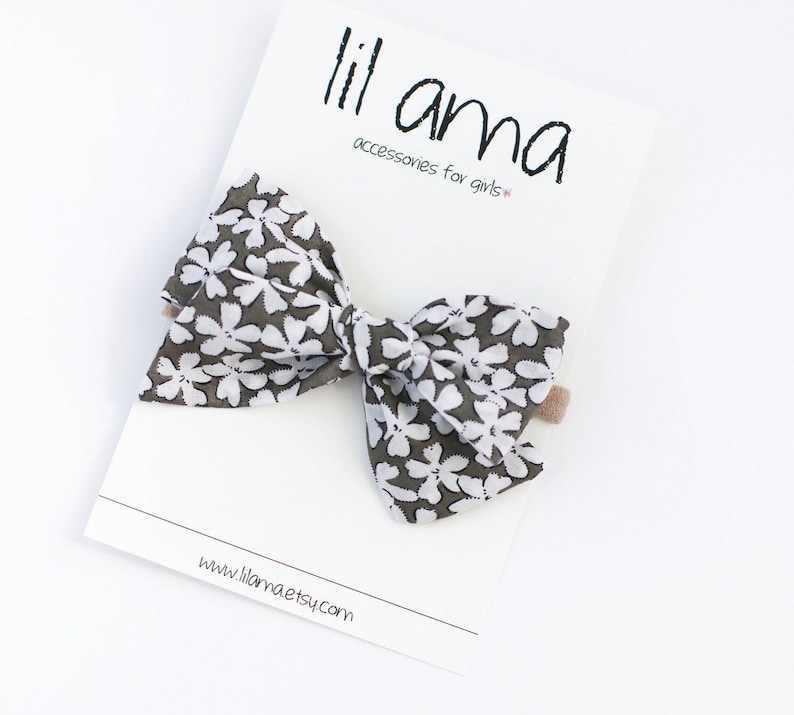 May include: A gray and white floral bow with a brown alligator clip. The bow is made of fabric and has a white floral pattern on a gray background. The bow is attached to a brown alligator clip. The bow is about 4 inches wide and 3 inches tall. The bow is perfect for adding a touch of style to any outfit.