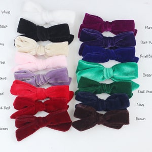 May include: A collection of velvet bows in various colors, including white, black, ivory, pink, mauve, red, dark red, maroon, plum, dark purple, royal blue, green, dark green, navy, and brown. Each bow is neatly arranged, showcasing the texture and color variations.