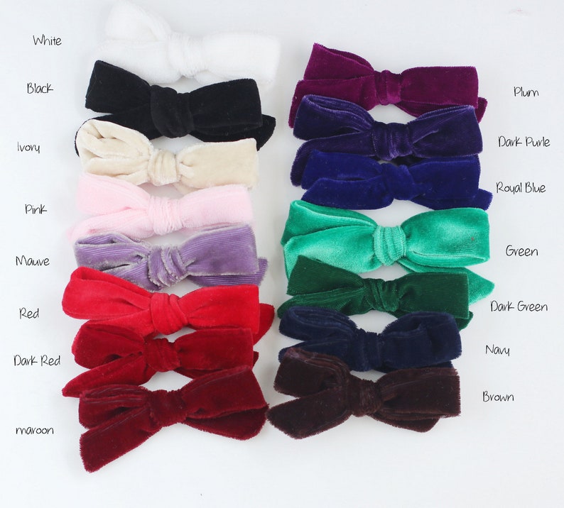 May include: A collection of velvet bows in various colors, including white, black, ivory, pink, mauve, red, dark red, maroon, plum, dark purple, royal blue, green, dark green, navy, and brown. Each bow is neatly arranged, showcasing the texture and color variations.
