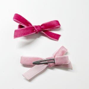 May include: Two velvet hair bows with clips. One bow is pink and the other is a darker shade of pink.