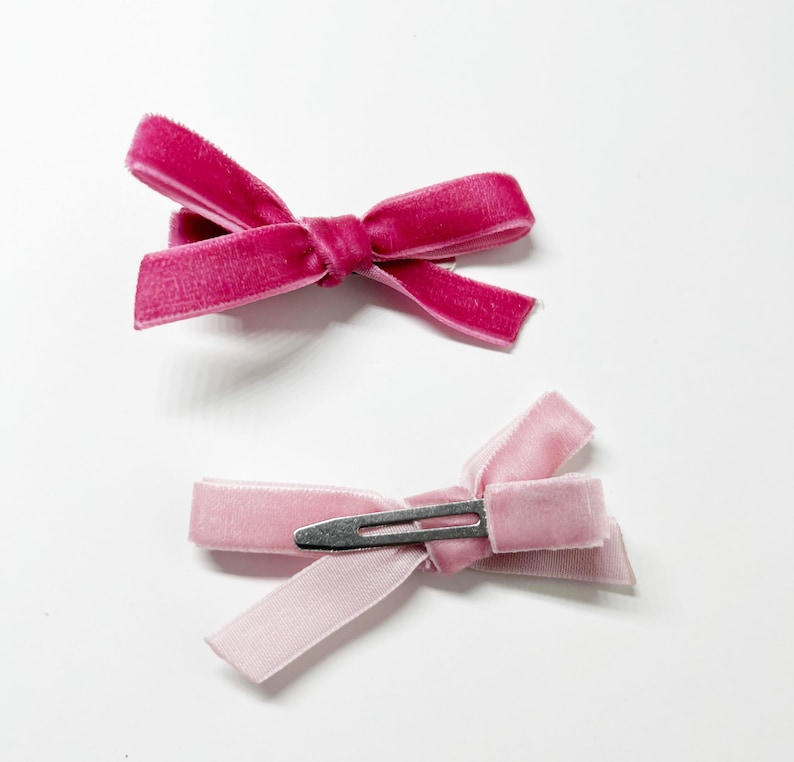 May include: Two velvet hair bows with clips. One bow is pink and the other is a darker shade of pink.