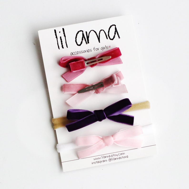 May include: A set of five velvet hair bows in pink, purple, and red, with two matching headbands. The bows are attached to alligator clips. The headbands are made of a thin, stretchy material. The card reads "lil ama accessories for girls" and includes the website and Instagram handle.
