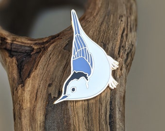 Puede incluir: Un pin de esmalte blanco y azul de un pájaro con cabeza negra y alas azules. El pájaro está mirando hacia la izquierda y está en posición de buceo.