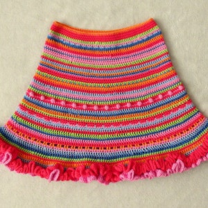 Op de afbeelding: Een kleurrijke gehaakte rok met een gerimpelde zoom. De rok is gemaakt met een verscheidenheid aan felle kleuren, waaronder roze, oranje, groen, blauw en geel.