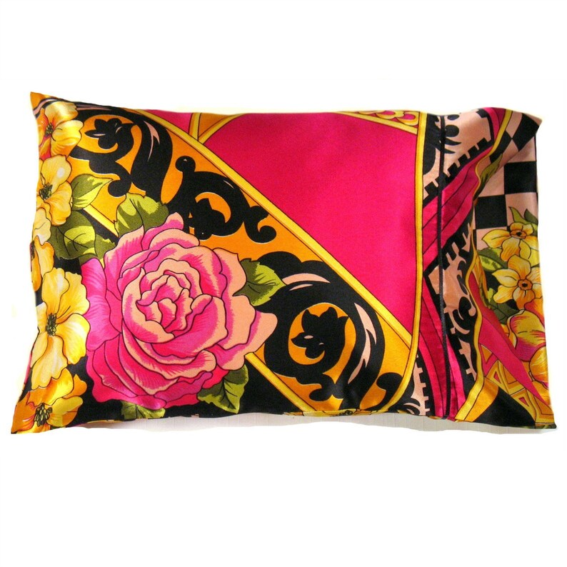 May include: A pink, yellow, and black patterned pillow with a floral design. The pillow is made of satin and has a decorative border.