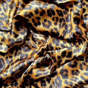May include: Close-up of a brown and black leopard print fabric with a satin finish. The fabric is draped and folded, creating a textured and luxurious look.