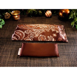 May include: A brown paisley patterned eye pillow with a solid brown eye pillow on a brown woven surface.