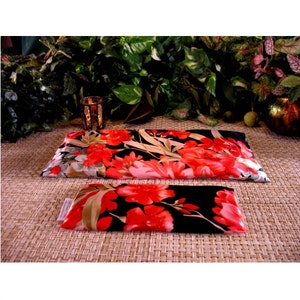 Pode incluir: Dois pacotes de calor retangulares com estampa floral, um maior que o outro. O pacote maior é de cor creme e preto com flores vermelhas, o pacote menor é preto com flores vermelhas. Ambos os pacotes estão sobre um tapete marrom tecido.