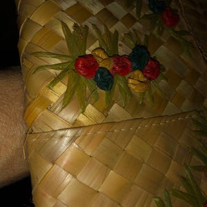 Pu&ograve; includere: Primo piano di un cappello di paglia intrecciata con un motivo floreale decorativo. Il cappello presenta un motivo a scacchi nei toni del beige e del marrone. Gli abbellimenti floreali includono accenti rossi, gialli e blu.