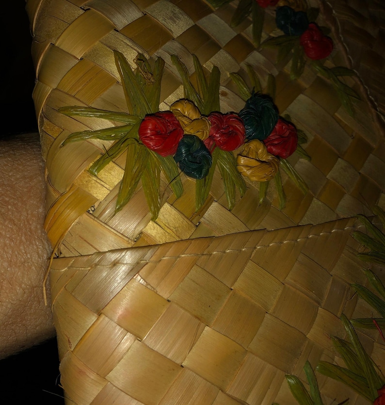 Pu&ograve; includere: Primo piano di un cappello di paglia intrecciata con un motivo floreale decorativo. Il cappello presenta un motivo a scacchi nei toni del beige e del marrone. Gli abbellimenti floreali includono accenti rossi, gialli e blu.