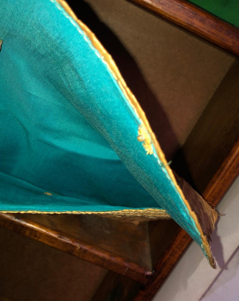 Pu&ograve; includere: Primo piano di una scatola di legno con fodera in tessuto turchese. Il tessuto ha un bordo dorato ed &egrave; parzialmente tirato indietro, rivelando l'interno. Il legno ha una finitura scura e ricca.
