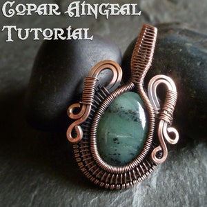 Puede incluir: Un colgante envuelto en alambre de cobre con una piedra preciosa verde. El colgante está sobre un fondo gris oscuro.