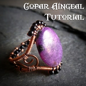 May include: A copper wire wrapped ring with a purple gemstone and black beads. The ring is on a dark grey surface. The text "COPAIR ÁINGÉAL TUTORIAL" is in the background.