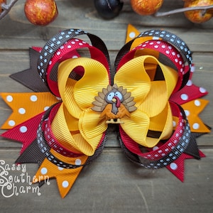 K&ouml;nnte beinhalten: Ein gro&szlig;er Haarschmuck in Herbstfarben. Der Haarschmuck besteht aus Schichten von gelben, orangefarbenen, roten und braunen B&auml;ndern, einige mit wei&szlig;en Punkten. Eine kleine Truthahn-Verzierung befindet sich in der Mitte. Wahrscheinlich handgefertigt.