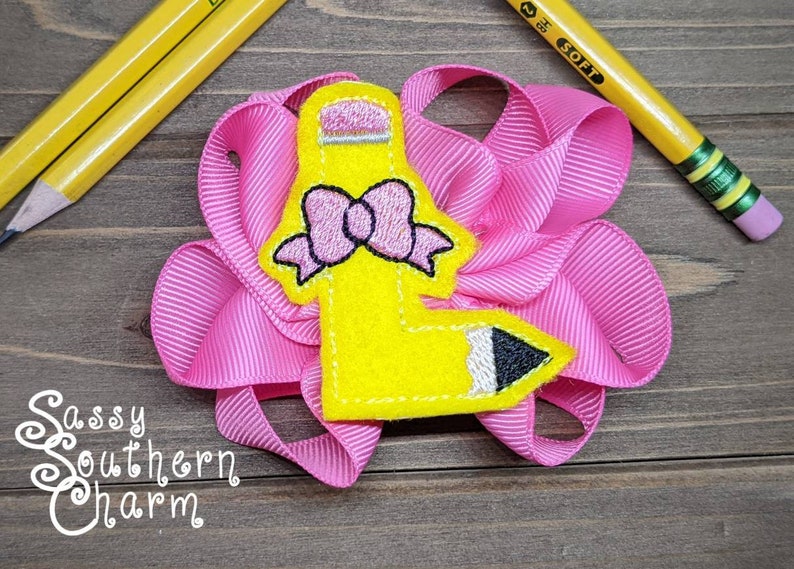 Op de afbeelding: Een gele viltstift met een roze strik en zwarte details, op een roze gerimpeld lint. De tekst "Sassy Southern Charm" is zichtbaar onder de stift.