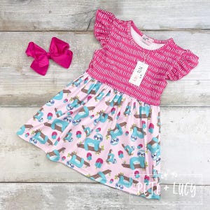 Puede incluir: Un vestido rosa con estampado de perezosos y un lazo rosa a juego. El vestido presenta un corpiño rosa con líneas verticales blancas y mangas con volantes. La falda tiene un fondo rosa claro con perezosos azules y ramas marrones.