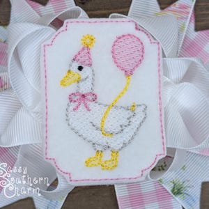 Puede incluir: Un motivo bordado de un ganso blanco con un gorro de fiesta rosa y un globo rosa. El ganso est&aacute; sobre un fondo blanco con un borde rosa, colocado sobre una cinta grande blanca y rosa. El texto "Sassy Southern Charm" es visible.