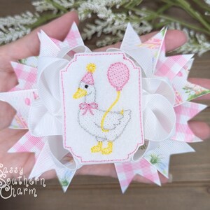 Puede incluir: Un lazo para el cabello hecho a mano con un dise&ntilde;o blanco y rosa. El lazo tiene un parche bordado central de un ganso con un gorro de fiesta y un globo rosa. El texto "Sassy Southern Charm" es visible.
