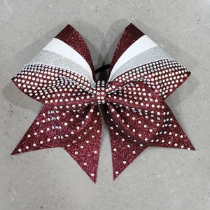 May include: A maroon cheer bow with white and silver stripes and rhinestones.