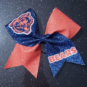 May include: A blue and orange glitter cheer bow with a bear head and the word "BEARS" in white letters.