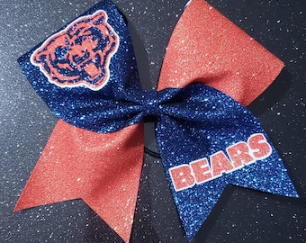 May include: A blue and orange glitter cheer bow with a bear head and the word "BEARS" in white letters.
