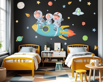 May include: Two yellow twin beds with white bedding and a blue and white patterned throw pillow. The beds are in a room with a black wall with a space-themed mural featuring three astronauts riding a rocket. The mural also includes stars, planets, and a UFO.