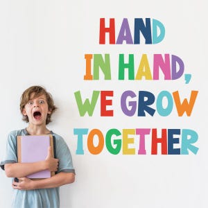Może przedstawiać: Młoda osoba z szeroko otwartymi oczami i otwartymi ustami trzyma książki przed białą ścianą. Na ścianie widnieje kolorowy tekst "HAND IN HAND, WE GROW TOGETHER" w różnych jasnych kolorach.