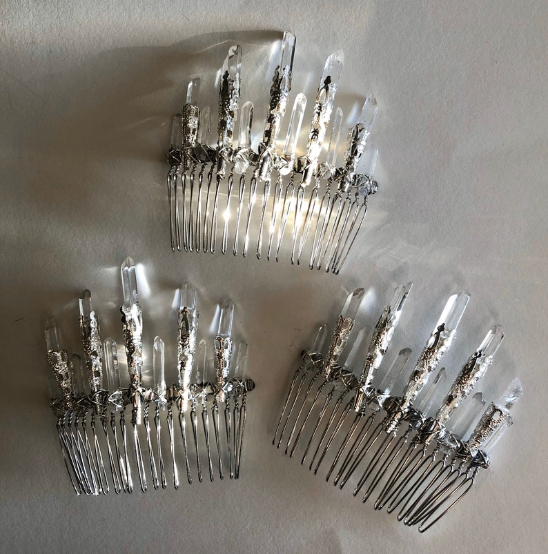 May include: Three silver hair combs with clear crystal accents. Each comb features a row of tines and is adorned with multiple crystal formations. The crystals are clear and faceted, catching the light. The combs are arranged on a light-colored surface.