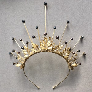 May include: A gold crown with black pearl accents and a delicate leaf design. The crown is made of wire and has a headband for wearing.