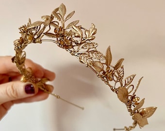 May include: A gold leaf crown headband with delicate floral details. The crown is made of wire and has a flexible band for a comfortable fit.