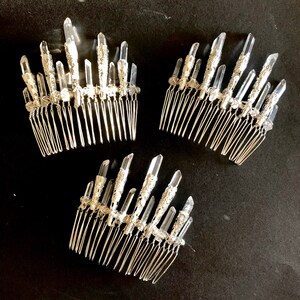 May include: Three silver hair combs with clear crystal accents are arranged on a black surface. Each comb features multiple crystal points and a decorative silver base, creating a sparkling, elegant look. The combs are designed for formal occasions.