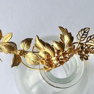 May include: A gold-colored floral crown with detailed leaves and flowers. The crown is made of metal and has a delicate, ornate design. The leaves and flowers are arranged around the band, creating a natural, elegant look.