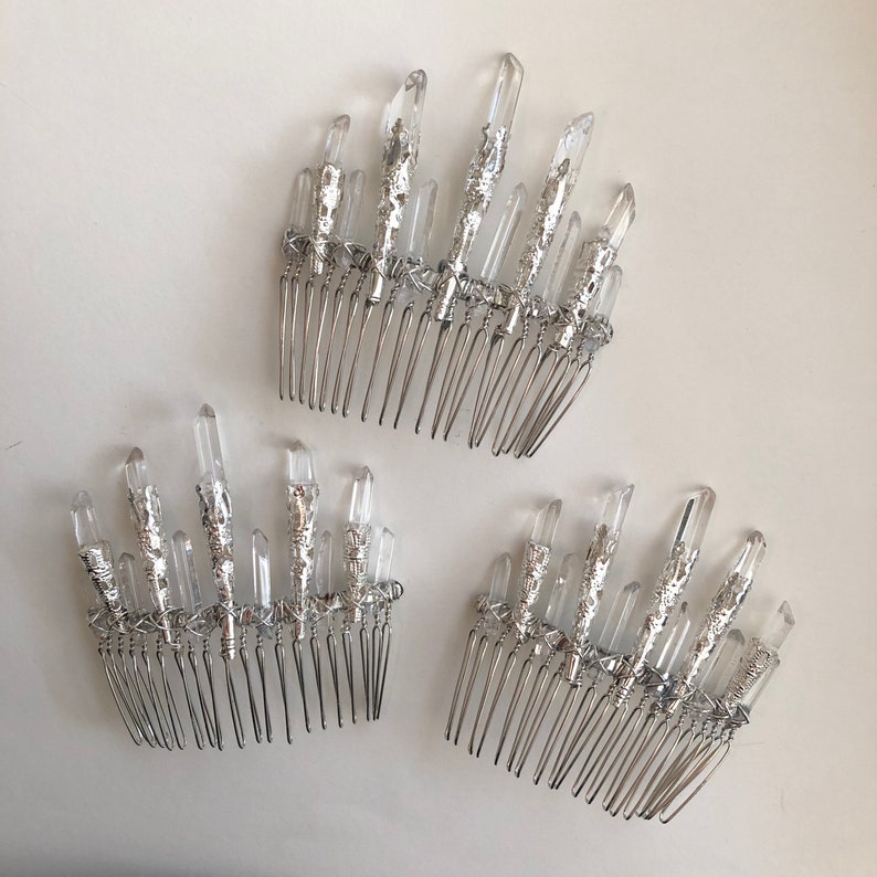 May include: Three silver hair combs with clear quartz crystal accents. The crystals are arranged in a fan shape and attached to the comb with silver wire. The combs are on a white background.