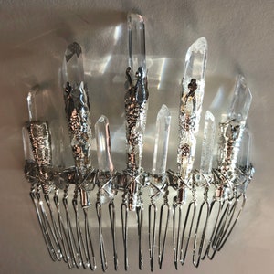 May include: A silver-toned hair comb adorned with clear quartz crystals. The crystals are of varying sizes and are set in ornate silver metalwork. The comb features multiple tines for securing in hair.