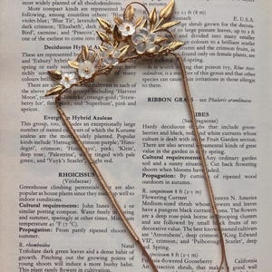 May include: A delicate gold-toned floral hair accessory with white flower accents and a slender, curved design. This elegant piece is likely for weddings or special occasions, adding a touch of vintage charm.