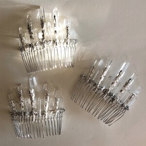May include: Three silver hair combs adorned with clear quartz crystals. The crystals are arranged in a vertical, spiky pattern, and the combs have a delicate, intricate design. The combs are displayed on a light-colored surface.