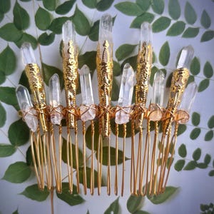 May include: A gold-colored hair comb adorned with clear quartz crystals. The comb features a series of tines and is embellished with gold filigree and wire. The crystals are of varying sizes and shapes, adding a natural, elegant touch.