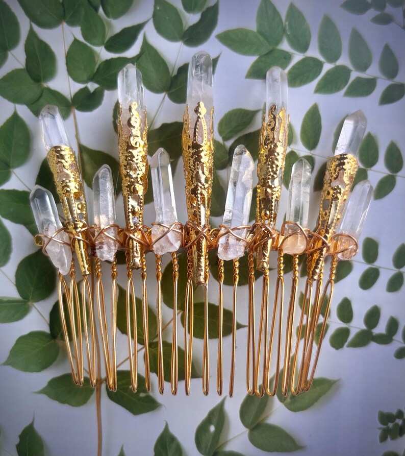May include: A gold-colored hair comb adorned with clear quartz crystals. The comb features a series of tines and is embellished with gold filigree and wire. The crystals are of varying sizes and shapes, adding a natural, elegant touch.