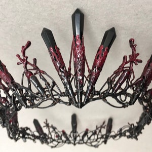 May include: A black metal crown with red accents and pointed black gemstones. The crown is intricately designed with a delicate wirework pattern.
