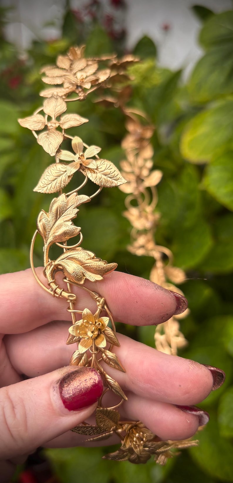May include: A gold-toned metal headpiece featuring a continuous vine design with intricate leaves and small flowers. The accessory is constructed from thin, flexible wire branches that connect the botanical elements in a repeating pattern.