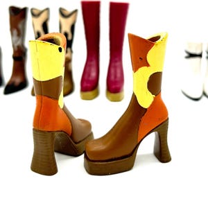 May include: A pair of platform boots with a brown, orange, and yellow color scheme. The boots have a chunky heel and a square toe. Several other pairs of boots in various styles and colors are in the background, including white, brown, and burgundy.