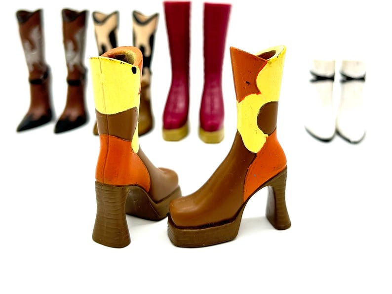 May include: A pair of platform boots with a brown, orange, and yellow color scheme. The boots have a chunky heel and a square toe. Several other pairs of boots in various styles and colors are in the background, including white, brown, and burgundy.