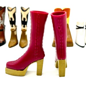 May include: A collection of miniature boots in various styles and colors. The foreground features a pair of bright pink platform boots with gold heels. Other boots include brown, white, and black cowboy boots, and a pair of white ankle boots.