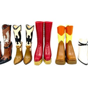 Könnte beinhalten: Eine Sammlung von Miniatur-Cowboystiefeln in verschiedenen Farben, darunter Braun, Schwarz, Rot und Weiß. Einige Stiefel weisen dekorative Elemente wie silberne Flügel und Sternmuster auf. Die Stiefel sind in einer Reihe vor weißem Hintergrund angeordnet.
