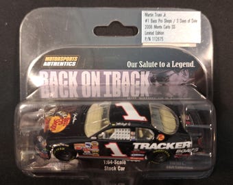 May include: A 1:64-scale black stock car in a clear plastic case. The car features the number 1 in white, along with various sponsor logos. Text on the packaging reads "Martin Truex Jr." and "Limited Edition."