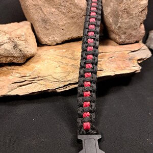 May include: A black and red paracord bracelet with a black plastic buckle.